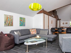 A modern living room with a gray sofa, a glass coffee table, and a brown bean bag. There are two abstract paintings on the wall, a wooden staircase, and a dining area with chairs. - Holiday Home in Ansager (Ansager)