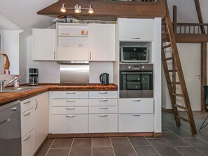Una cocina compacta con armarios blancos, horno empotrado y cafetera.