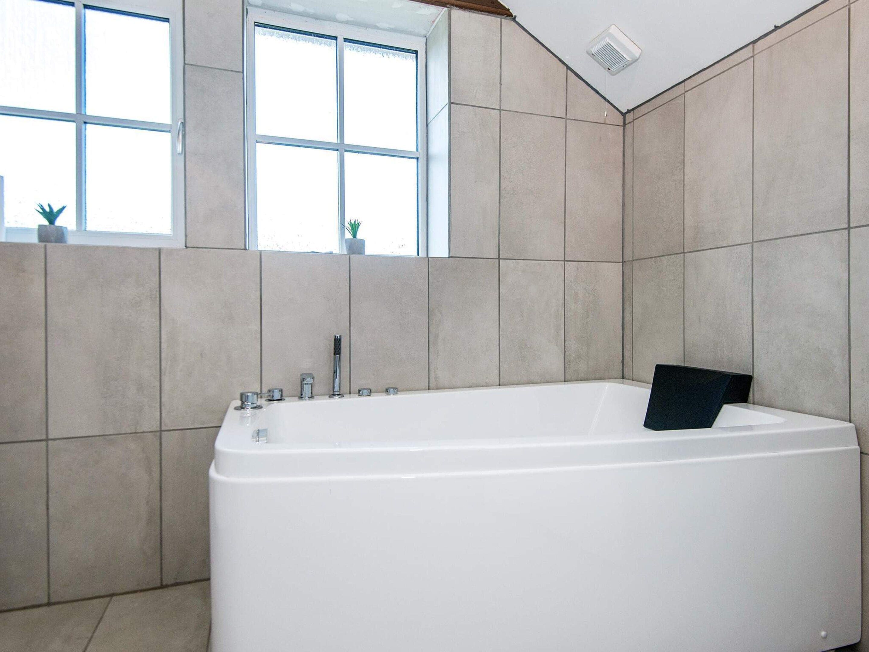 A modern bathroom with a freestanding bathtub, a window with a view, and tiled walls.