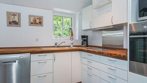 Una cucina moderna con mobili bianchi, un piano di lavoro in legno, una lavastoviglie, una macchina da caffè e una finestra con vista sul verde.