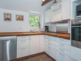 A modern kitchen with white cabinets, a wooden countertop, a dishwasher, a coffee maker, and a window with a view of greenery.