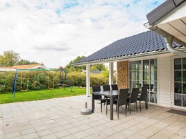 A covered patio area with a table and chairs, a swing set, and a stone pillar.