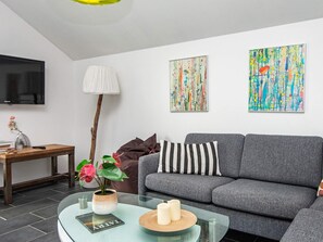 Una sala moderna con un sofá gris, una mesa de centro de vidrio, un televisor montado en la pared y dos cuadros abstractos.
