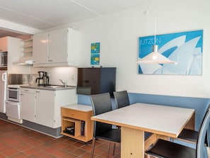 A compact kitchenette with a coffee maker, a microwave, and a stove. There is a dining area with a table and chairs, and a bench. A TV is mounted on the wall, and artwork is displayed above it.