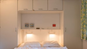 A bedroom with a bed, two bedside tables, a wardrobe, and wall-mounted lights. - 4 Person Holiday Home in Fano (Fano)