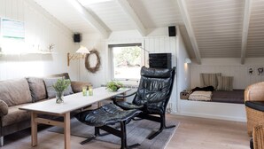 A cozy loft-style room with a high ceiling, a wooden table, a leather chair, a sofa, and a window with a view of greenery. - 4 Person Holiday Home in Fano (Fano)