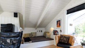 A cozy room with a sloped ceiling, a black leather chair, a wicker sofa, and a wooden table. - 4 Person Holiday Home in Fano (Fano)