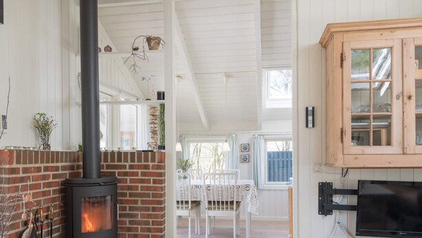 A cozy room with a brick fireplace, a wooden cabinet with glass doors, and a television mounted on the wall. - 4 Person Holiday Home in Fano (Fano)