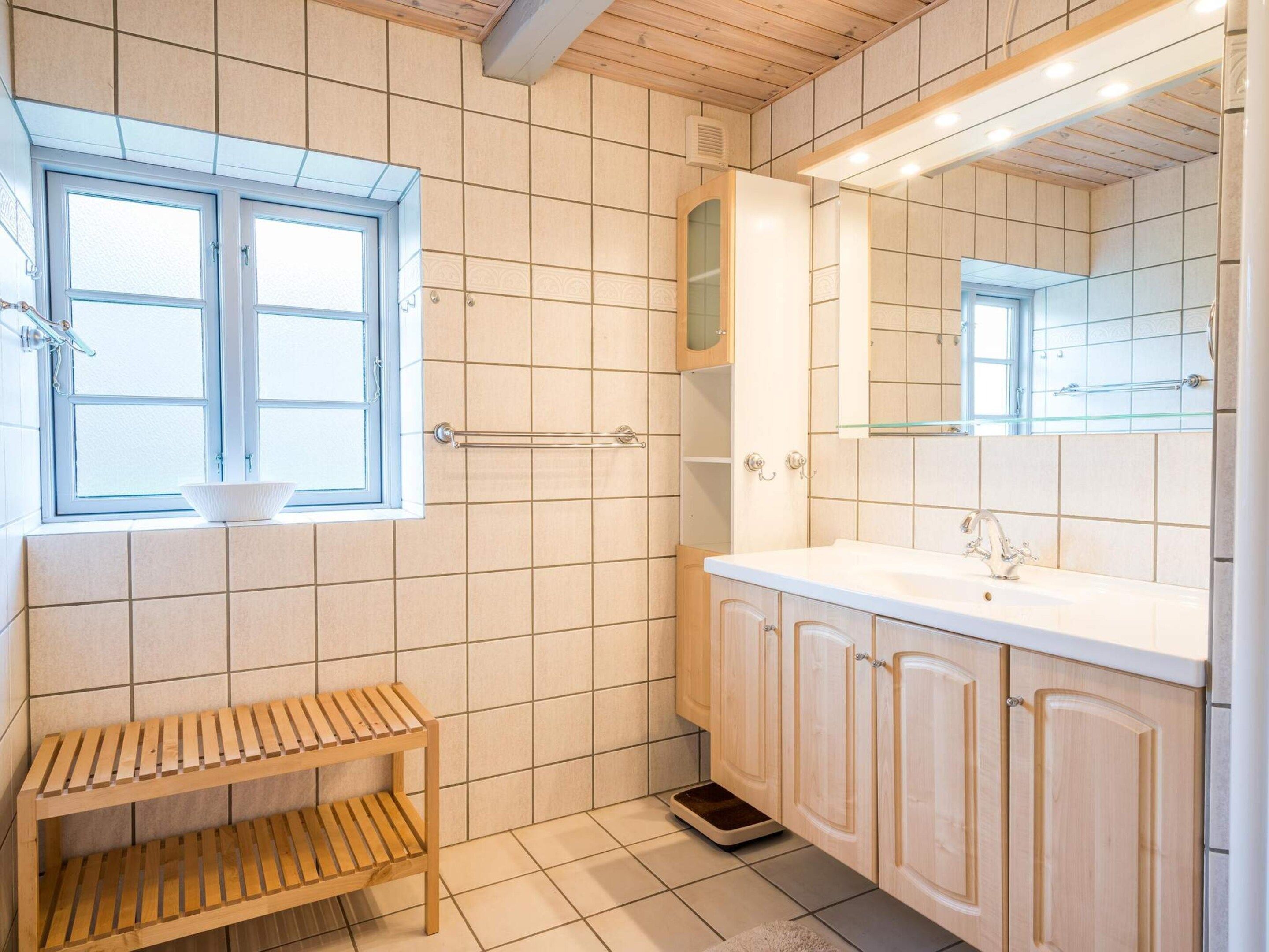 Un bagno con finestra, un lavabo, armadietti e uno scaffale in legno.
