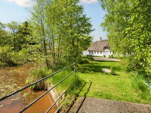 A rural house with a thatched roof, surrounded by lush greenery and a small stream.