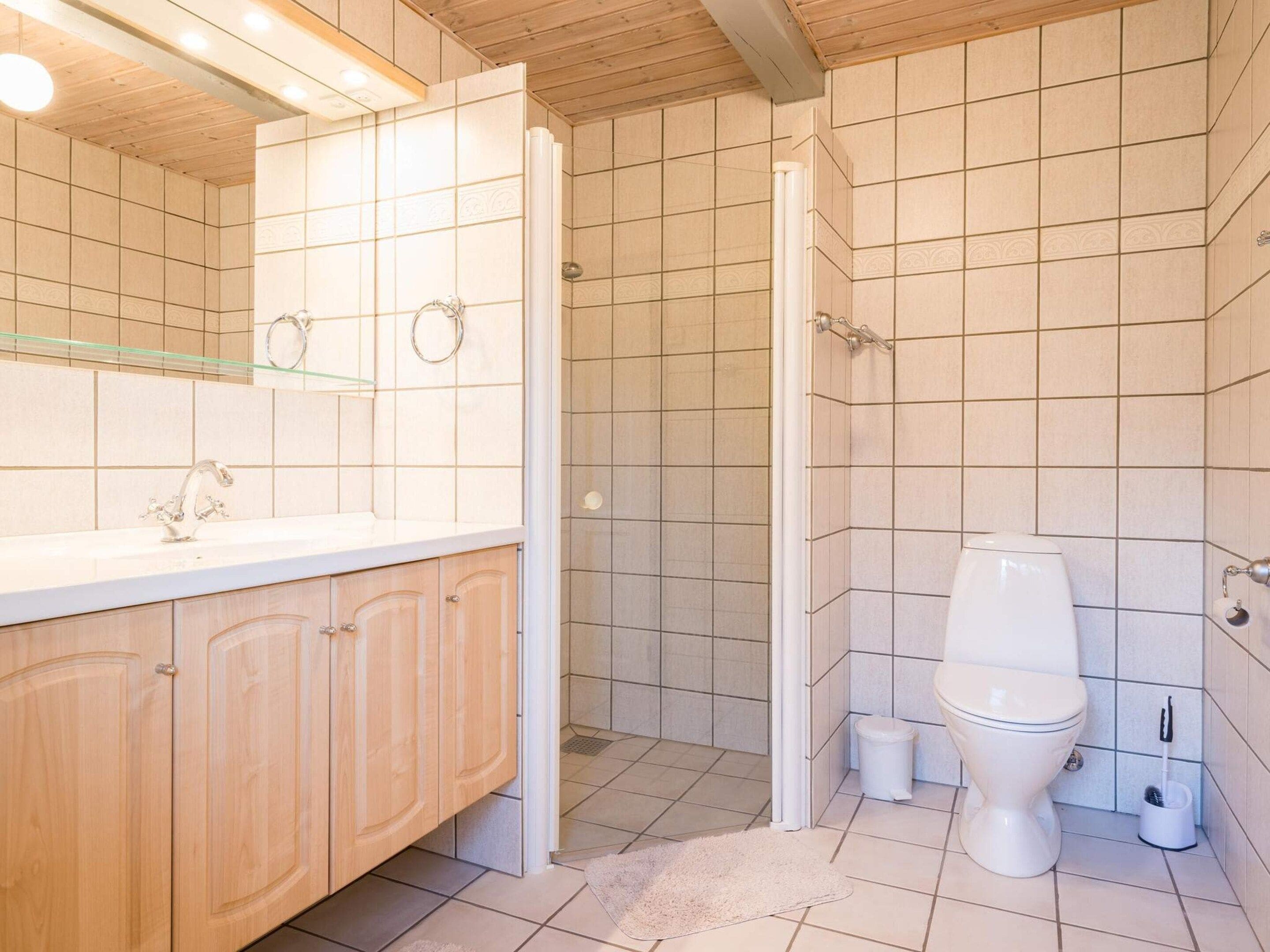 A bathroom with a wooden vanity, a toilet, and a shower area.