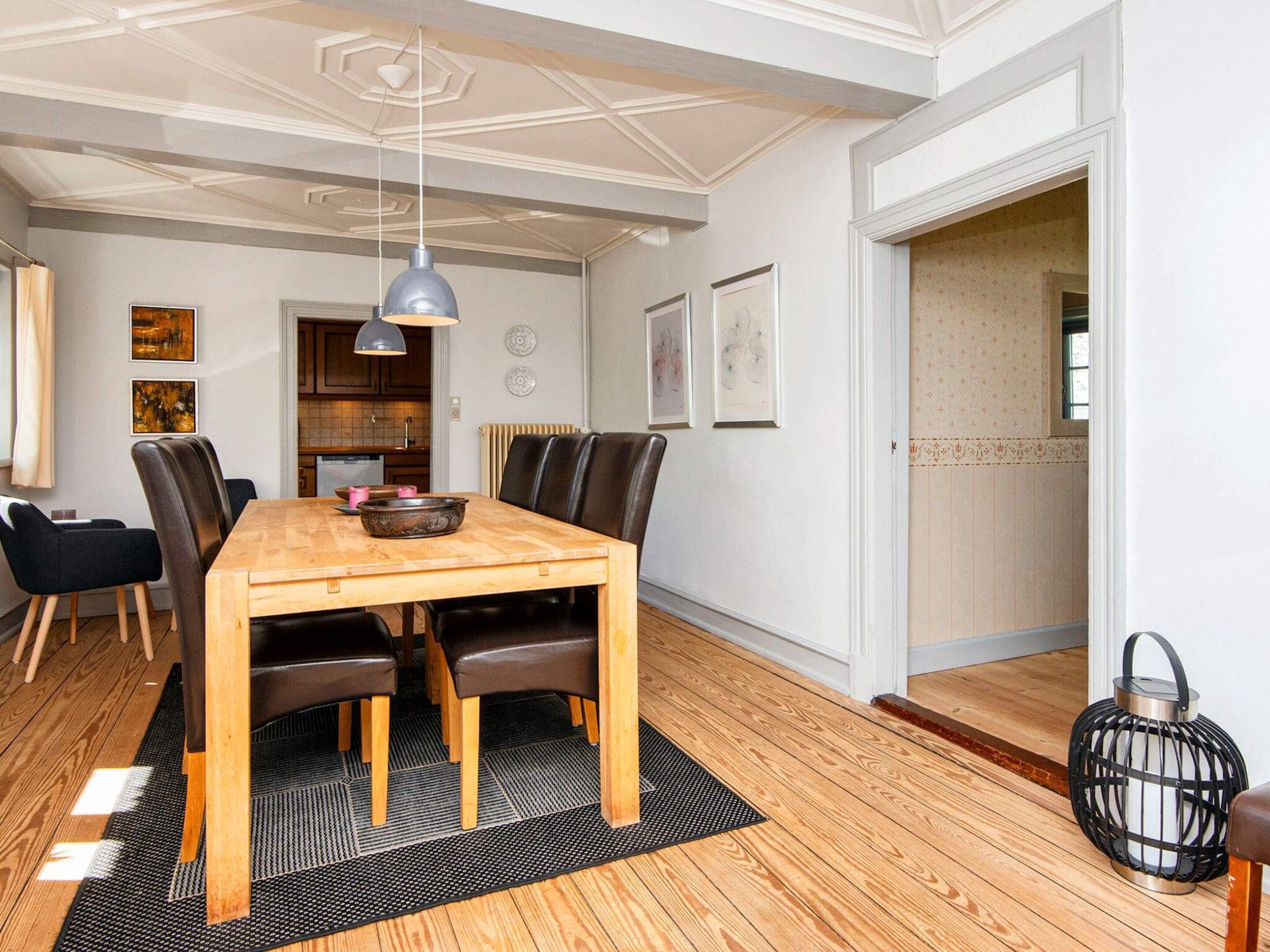 Een eetgedeelte met een houten tafel, zwarte stoelen, een zwart tapijt en een hanglamp.