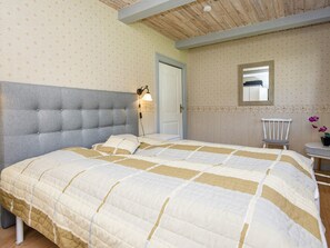 A bedroom with a large bed, a nightstand, a chair, a wall-mounted light, and a door.