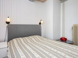 Un dormitorio con una cama grande, dos lámparas de noche, un radiador y una pequeña mesa con un objeto rojo encima.