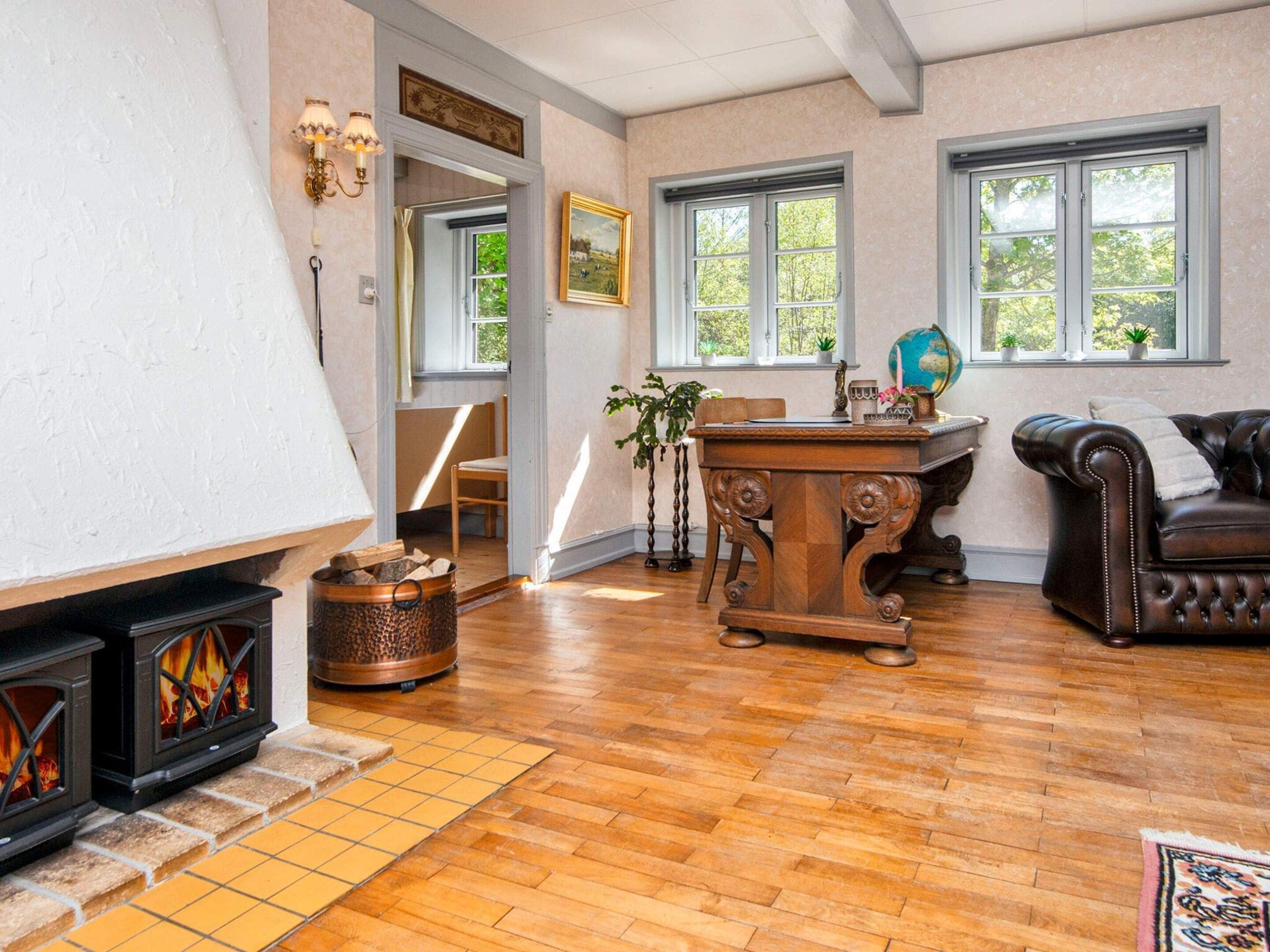 Una sala de estar acogedora con chimenea, suelo de madera, un sofá de cuero y un escritorio con un globo terráqueo.