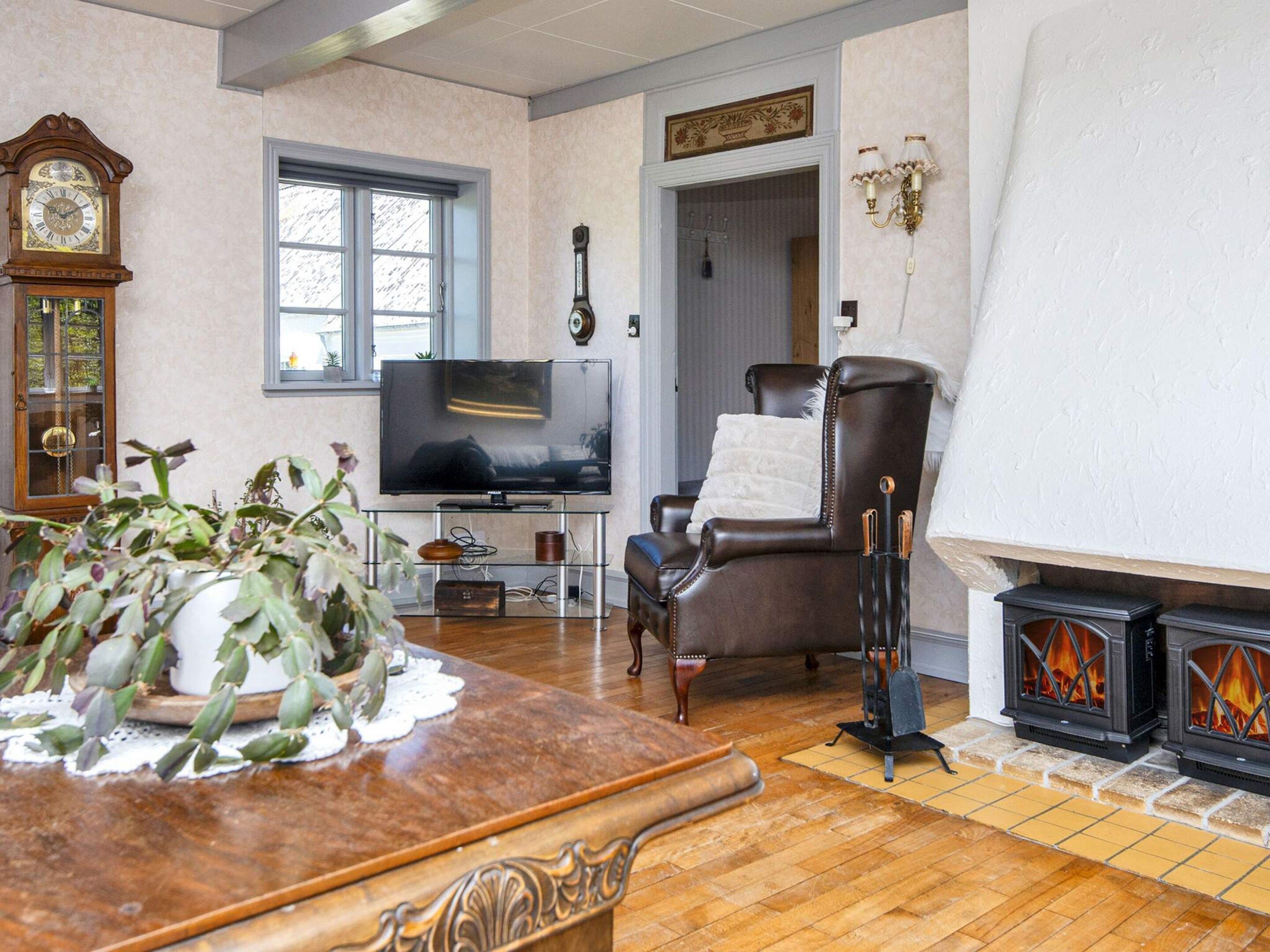 Una sala de estar con televisor, chimenea, reloj y ventana.