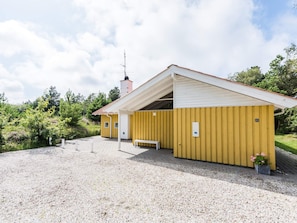 Un bâtiment jaune avec un toit blanc, une cheminée et un banc à l’extérieur.