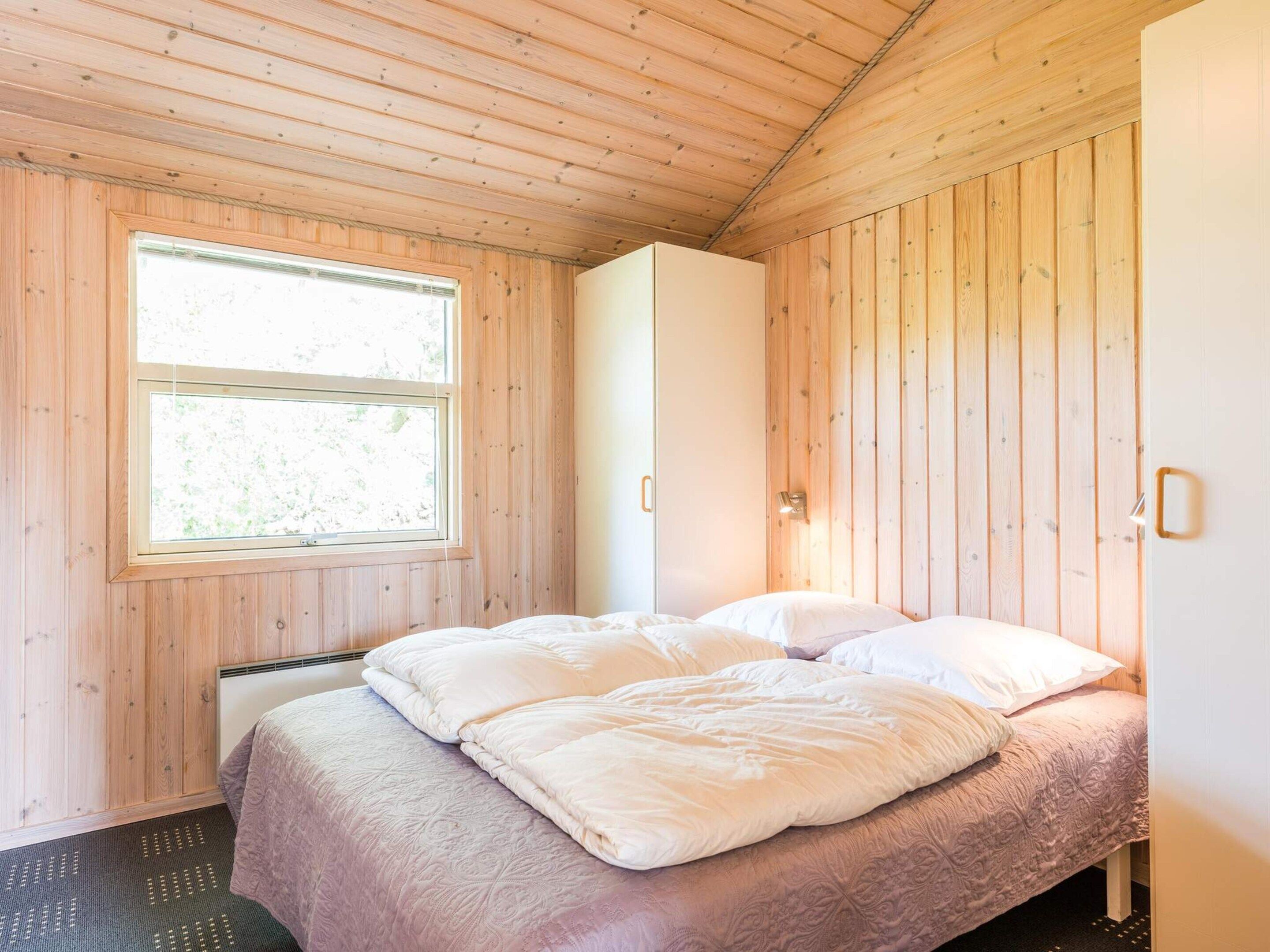 A bedroom with a wooden ceiling, a bed with white bedding, a window, and a white wardrobe.