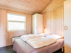 Ein Schlafzimmer mit Holzboden, einem Bett mit weißer Bettwäsche, einem Fenster und einem weißen Kleiderschrank.
