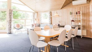 A room with a wooden ceiling, a round table with chairs, a sofa, a bookshelf, and large windows. - 4 Star Holiday Home in Henne (Henne)