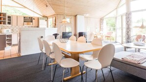 A modern interior with a wooden ceiling, a dining area with a large table and chairs, a kitchen with built-in cabinets, and large windows providing natural light. - 4 Star Holiday Home in Henne (Henne)