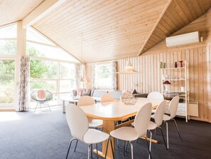 A modern interior with a wooden ceiling, a round dining table with chairs, a sofa, and a bookshelf. - 4 Star Holiday Home in Henne (Henne)