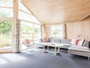 Relax in this stylish room with a high ceiling, open-plan layout, and large windows offering a view of lush greenery.