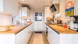 A modern kitchen with white cabinetry, wooden countertops, a built-in oven, and a large window. - Holiday Home in Henne (Henne)