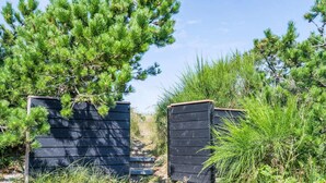 A pathway leading to a wooden structure surrounded by pine trees and shrubs. - Holiday Home in Henne (Henne)