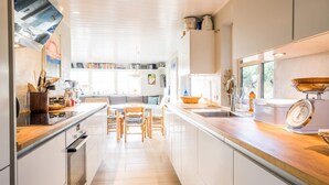 A modern kitchen with white cabinetry, a central island, and a dining area with wooden chairs. - Holiday Home in Henne (Henne)