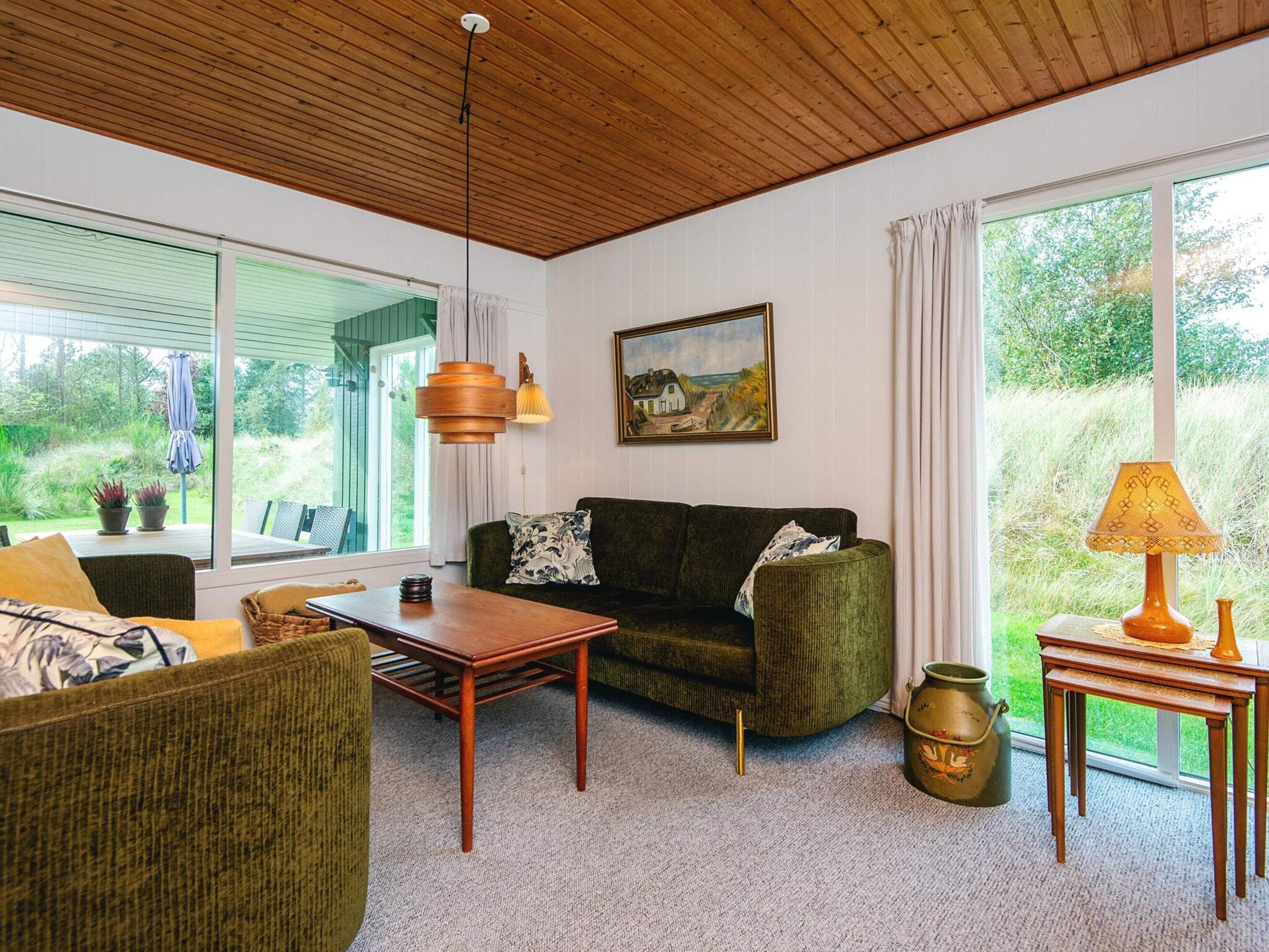 A cozy living room with a wooden ceiling, a green sofa, a wooden coffee table, and a painting on the wall.