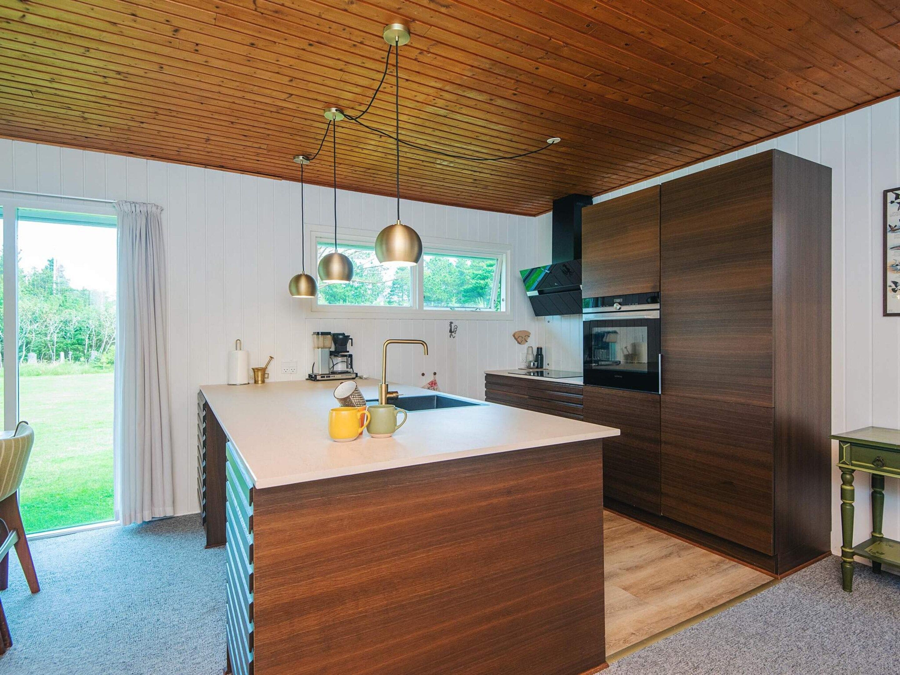A modern kitchen with a large island, wooden cabinets, and pendant lighting.