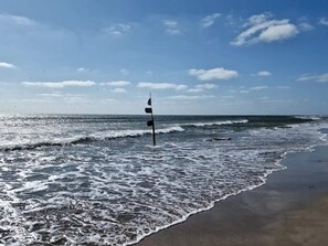 A beach with waves, a flag, and a clear sky. - 6 Person Holiday Home in Blavand (Blavand)
