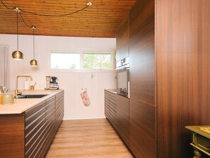 A modern kitchen with wooden cabinets, a built-in oven, and pendant lighting. - 6 Person Holiday Home in Blavand (Blavand)