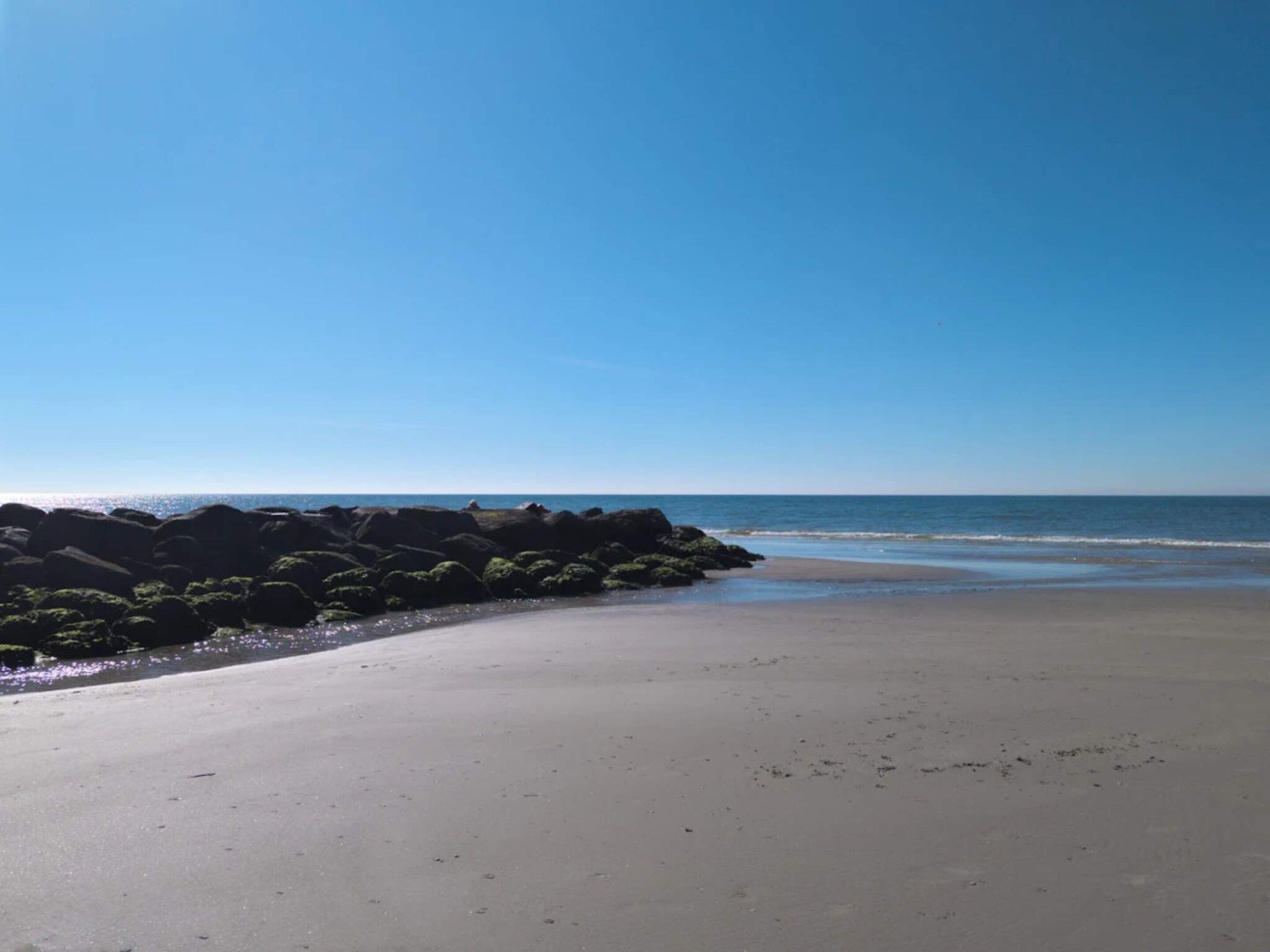 A beach with a clear sky, calm sea, and rocky outcrops.
