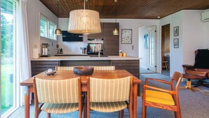 Une cuisine moderne avec un plafond en bois, un coin repas avec des chaises à rayures et une grande fenêtre.