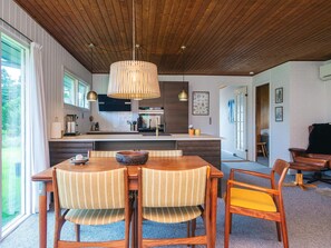 A modern kitchen with a wooden ceiling, a dining area with striped chairs, and a large window. - 6 Person Holiday Home in Blavand (Blavand)