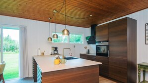 Une cuisine moderne avec un plafond en bois, des luminaires suspendus, un îlot central et une grande fenêtre.