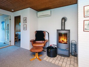 A cozy room with a leather chair, a wood-burning stove, and a white brick wall. - 6 Person Holiday Home in Blavand (Blavand)