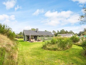 A single-story house with a covered patio, surrounded by a grassy yard and dense shrubbery. - 6 Person Holiday Home in Blavand (Blavand)