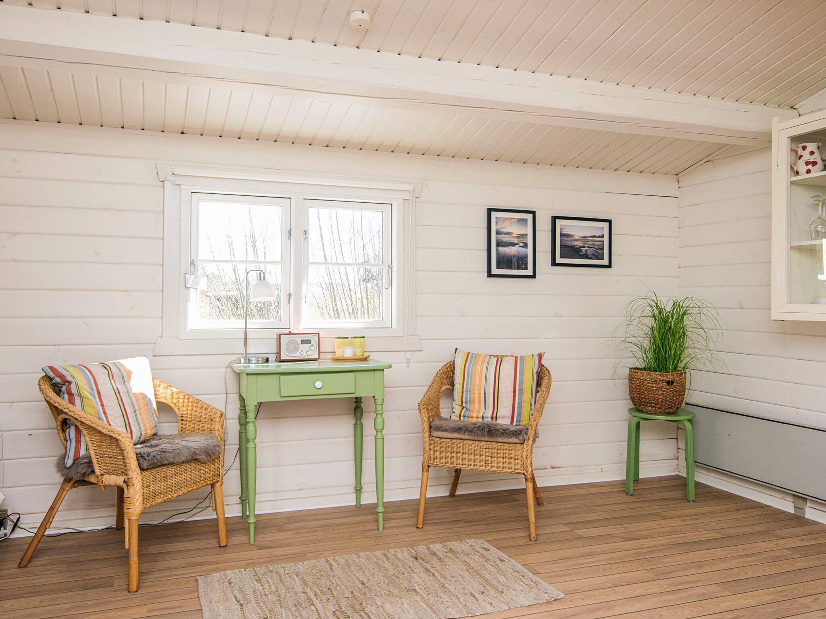 A cozy room with two wicker chairs, a small green table, and a window with two framed pictures.