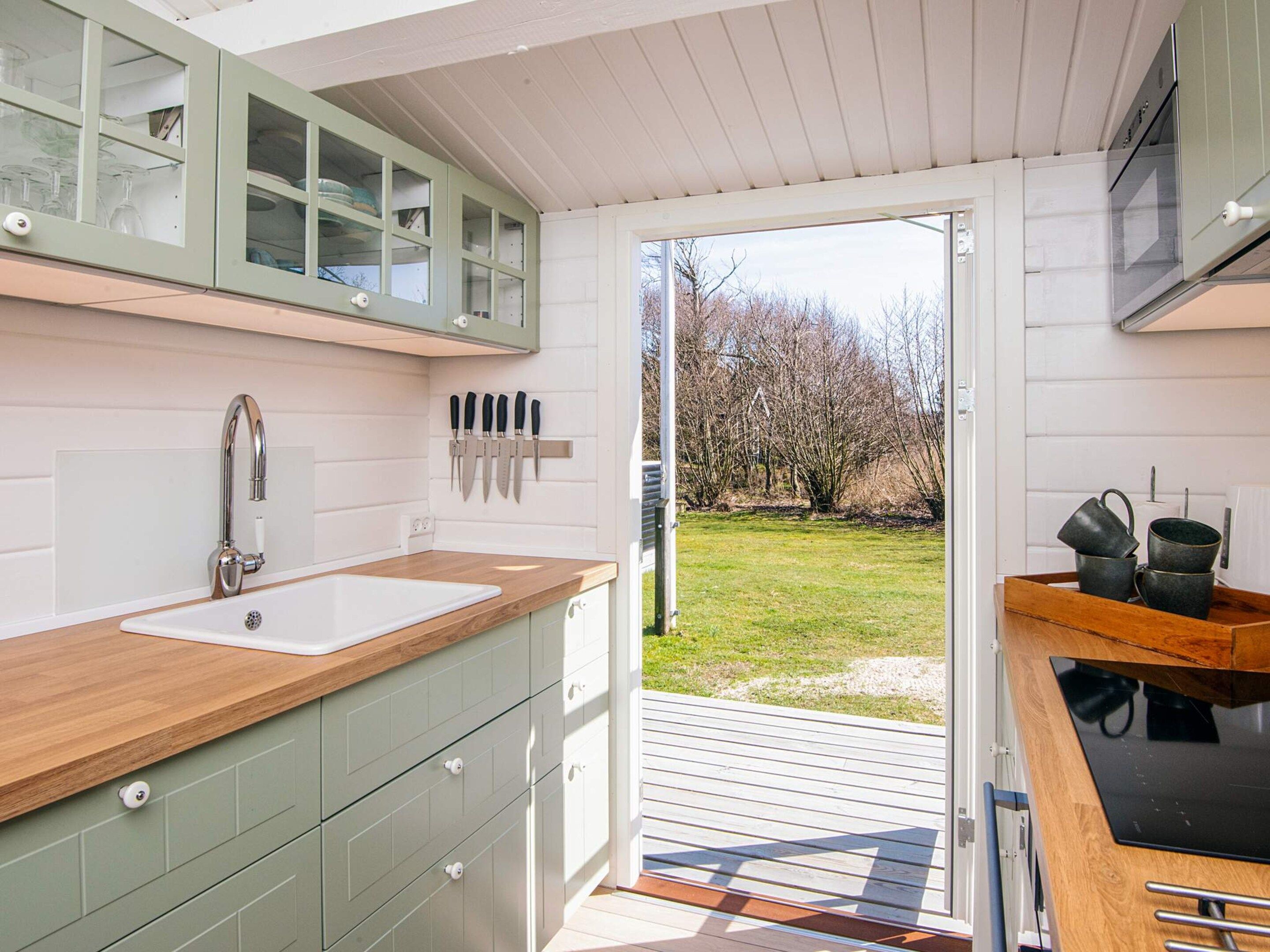 A kitchen with a wooden countertop, a sink, and a window overlooking a grassy area.