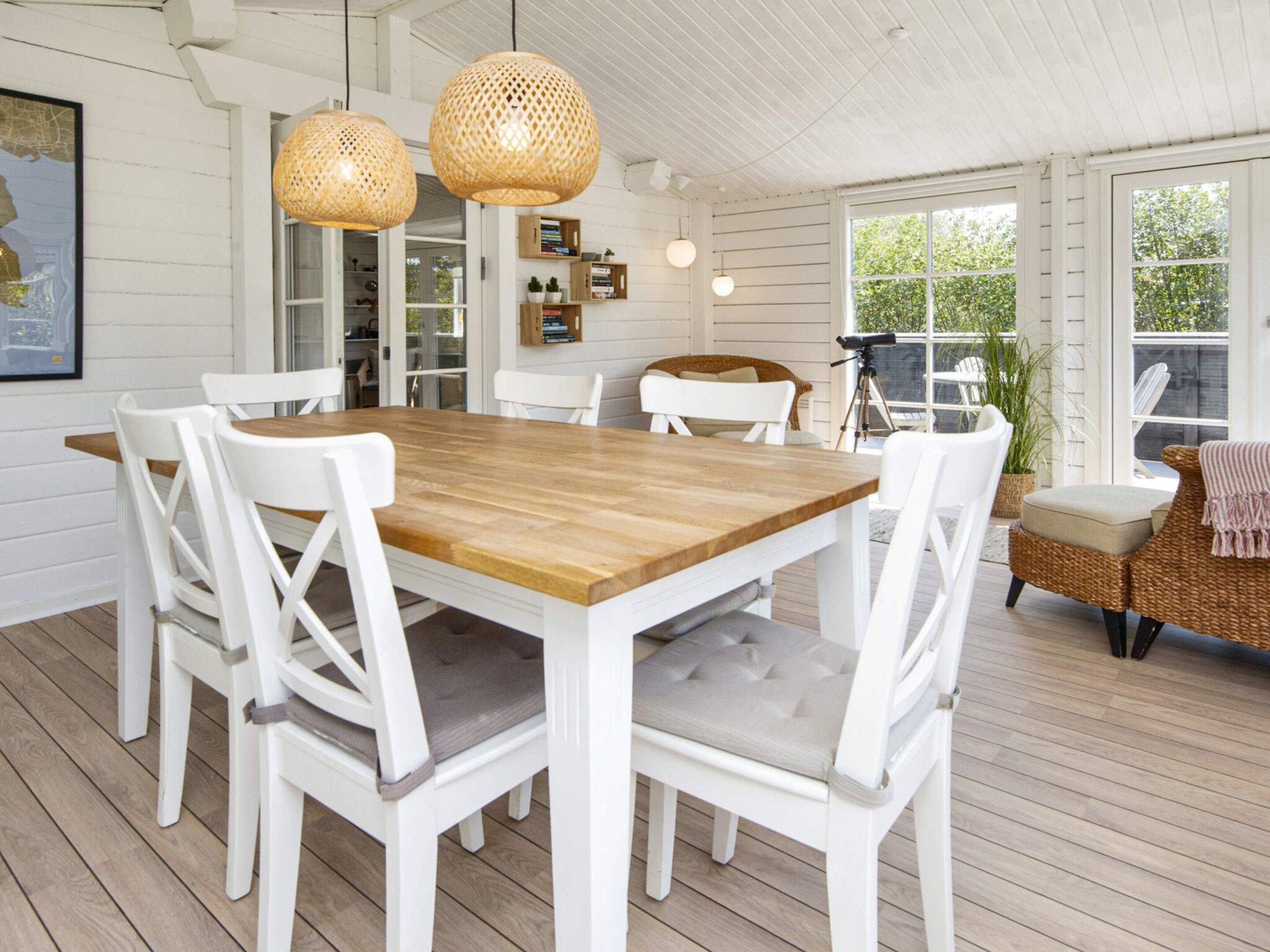 A dining area with a wooden table and white chairs, a wicker chair, and a telescope on a deck.