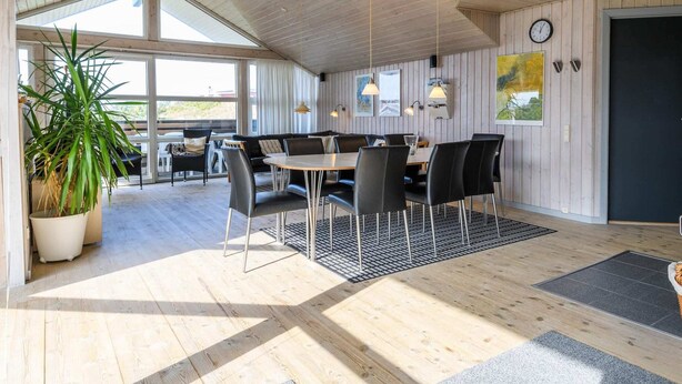 A spacious room with a wooden ceiling, a large dining table with chairs, a sofa, and a potted plant.