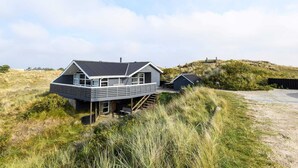 A modern house with a sloped roof, large windows, and a balcony overlooking a grassy landscape.