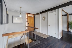 A modern interior with a wooden staircase, a framed picture, a decorative wall piece, and a door with a wooden panel.