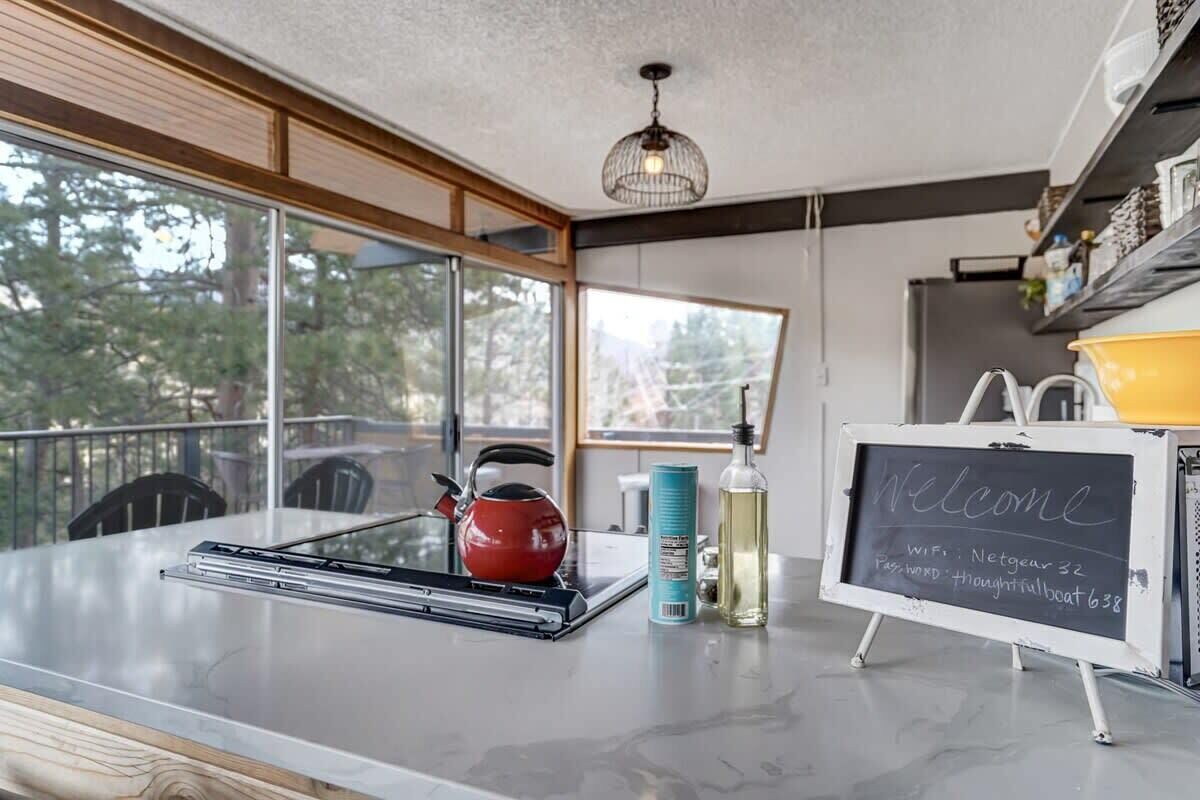Una cucina moderna con un'ampia finestra, un bollitore rosso, una lavagna con informazioni sul Wi-Fi e un contenitore giallo.