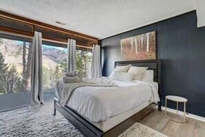 Een slaapkamer met een groot bed, uitzicht op bomen door het raam, en een schilderij aan de muur.