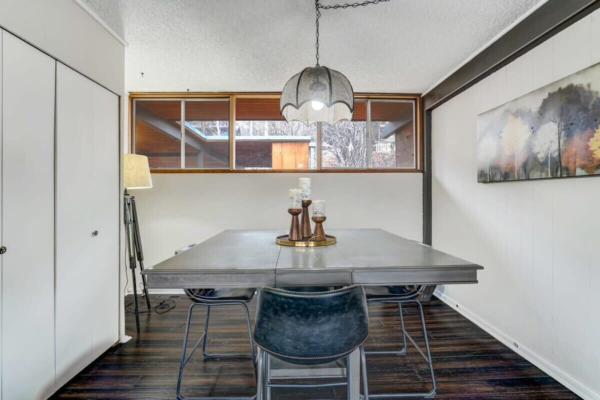 A dining area with a large table, two chairs, a hanging light fixture, and a window with a view.