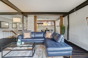 Un salon moderne avec un canapé d’angle en cuir bleu, une table basse en verre et un tapis à motifs.
